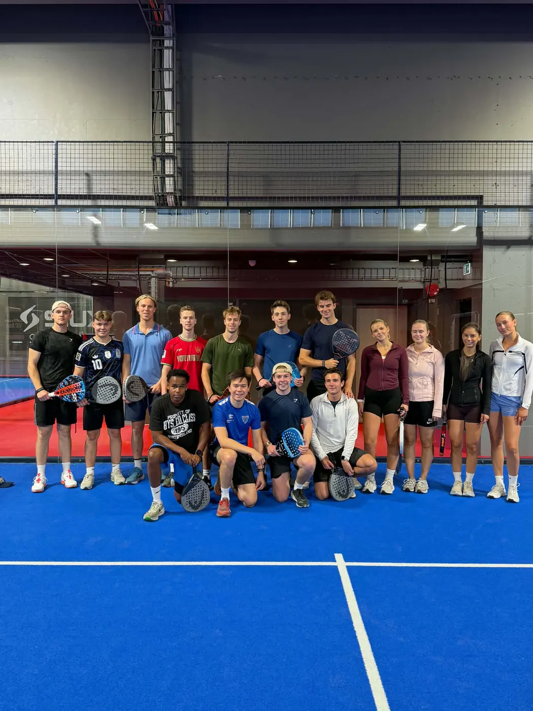 Stor gruppe studenter som poserer sammen på en padelbane etter trening