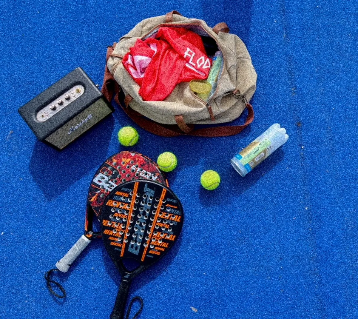Racketer, baller og en treningsbag liggende på en blå padelbane